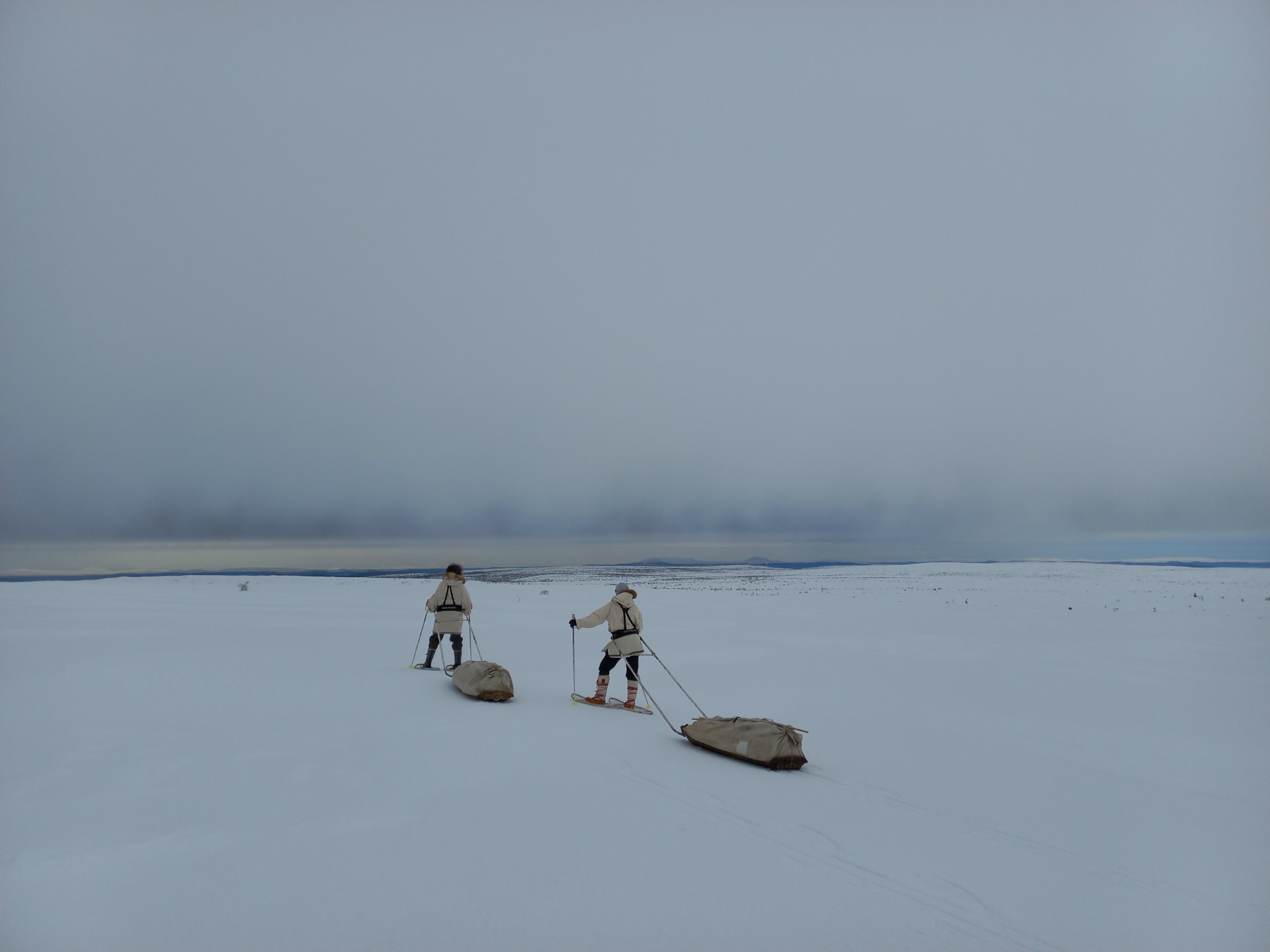 Twee mensen trekken pulka's door een eindeloze, lege sneeuwvlakte in Zweeds Lapland