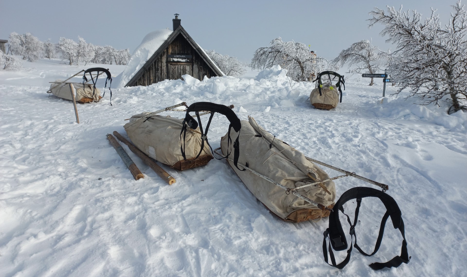 Pulka's liggen in de sneeuw voor een houten hutje in Zweeds Lapland